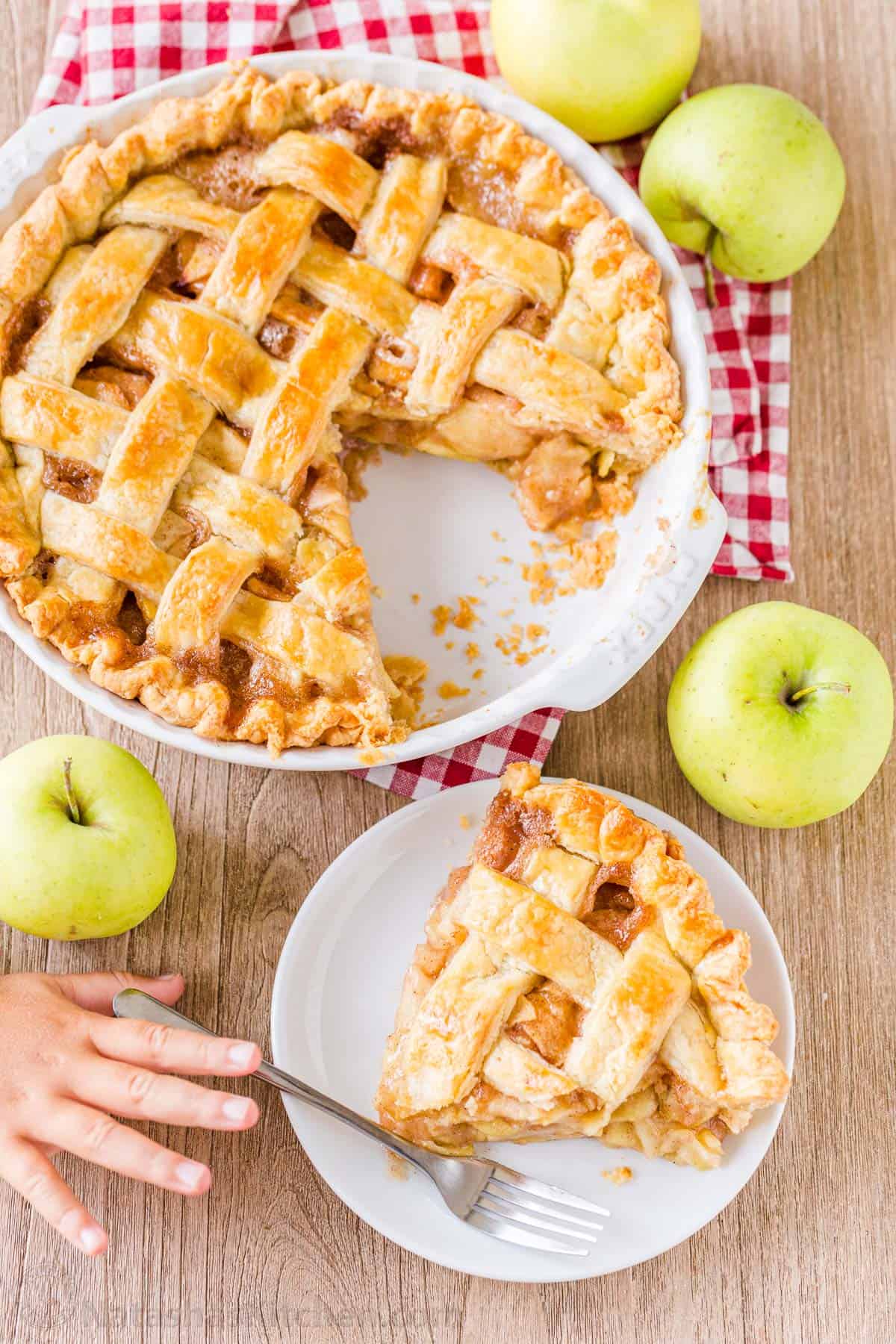 Apple pie served on a plate with hand reaching for fork