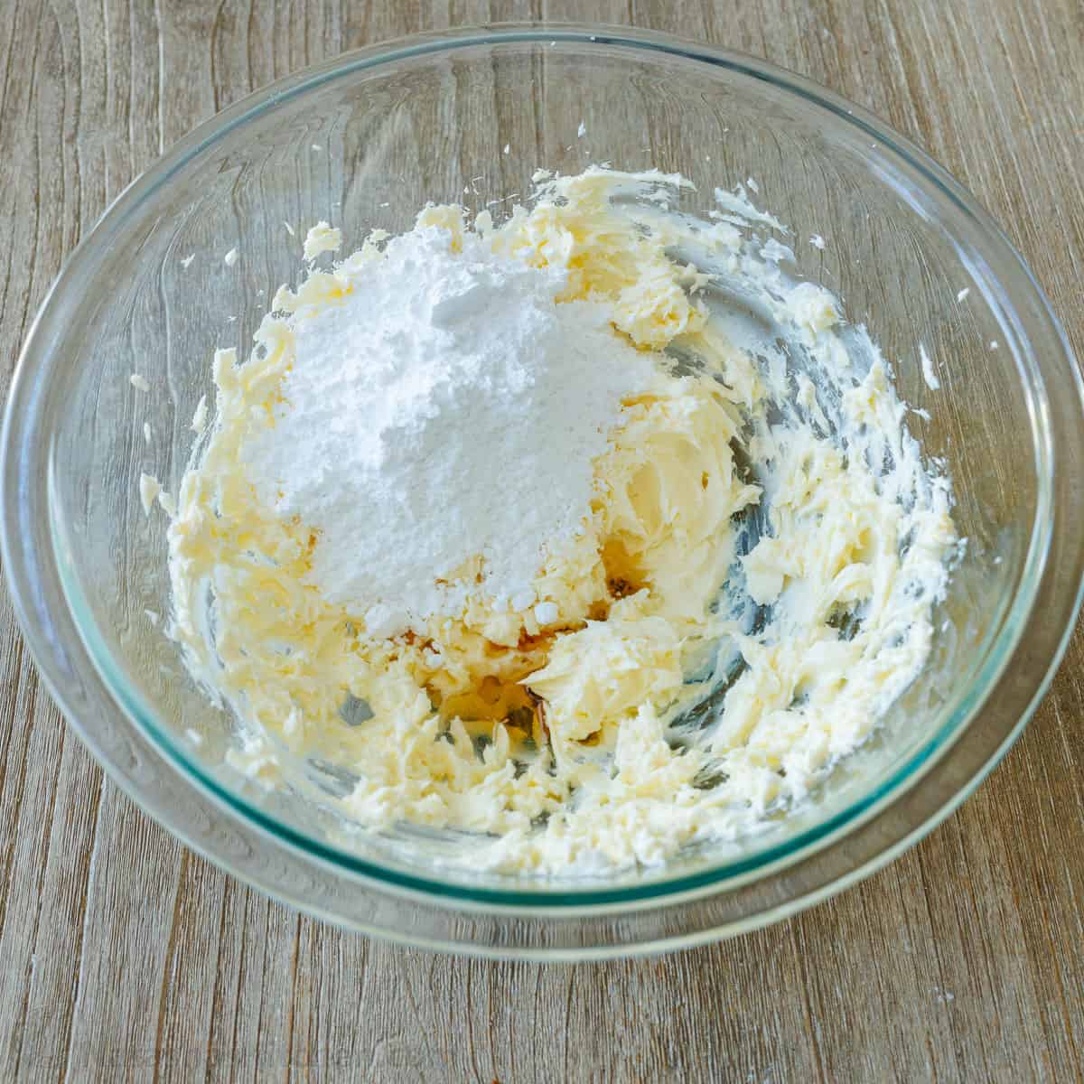 Creamed butter and cream cheese with powdered sugar in a glass bowl