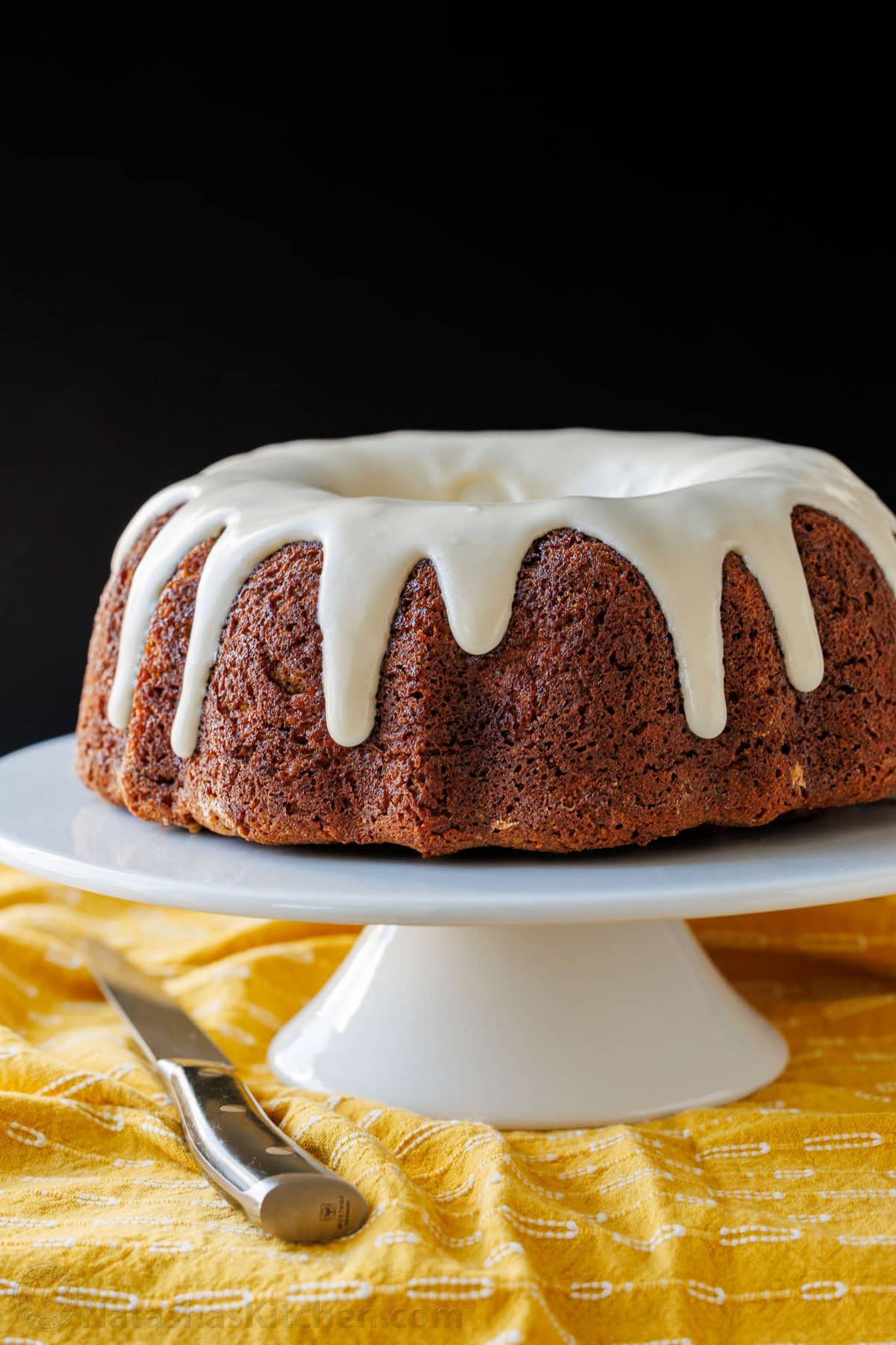 Banana Bundt Cake with Cream cheese glaze on a pedestal with a knife