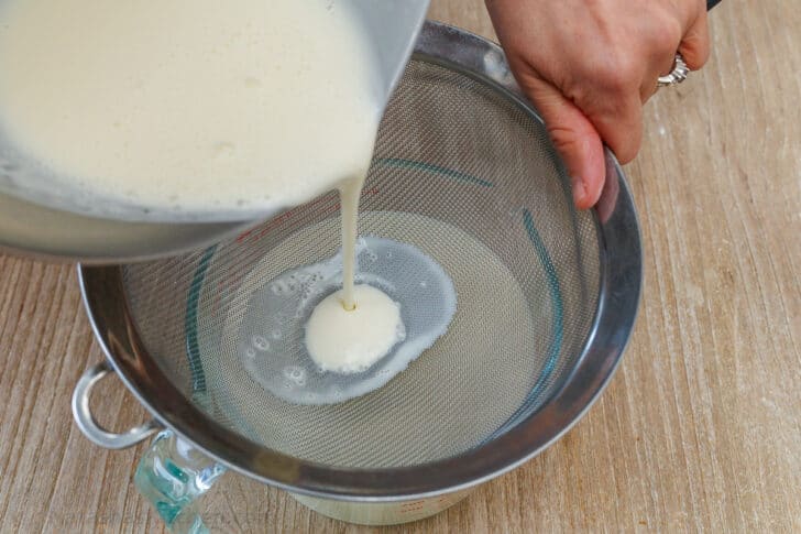 Pouring the mixture through a fine strainer, into a glass bowl with pouring lip, to remove any lumps