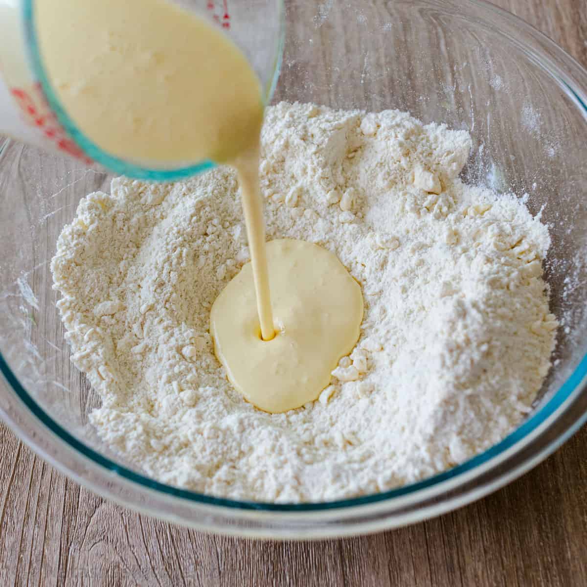 heavy cream poured into a bowl of flour for making homemade biscuits