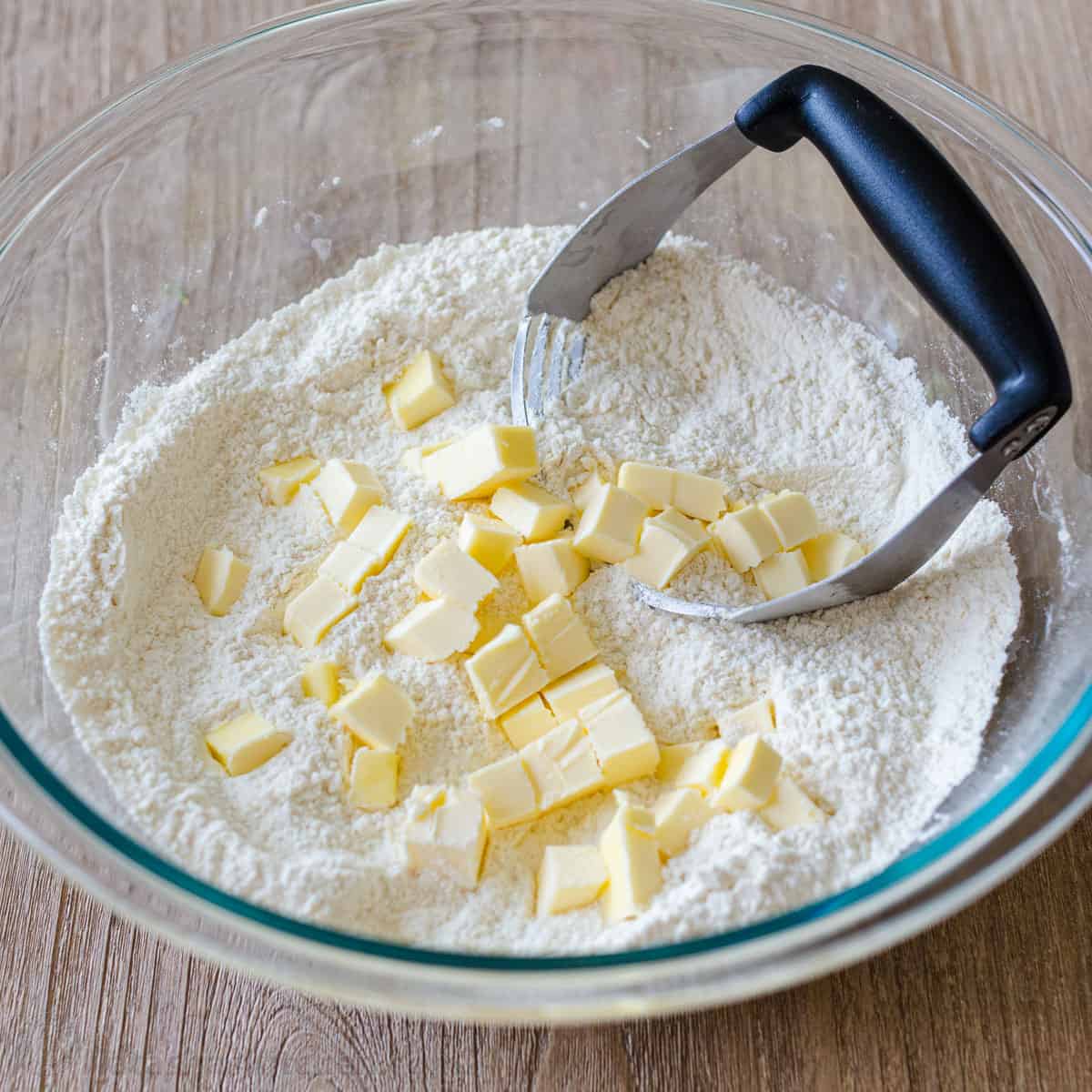 cubes of butter and flour in a clear bowl with a pastry cutter