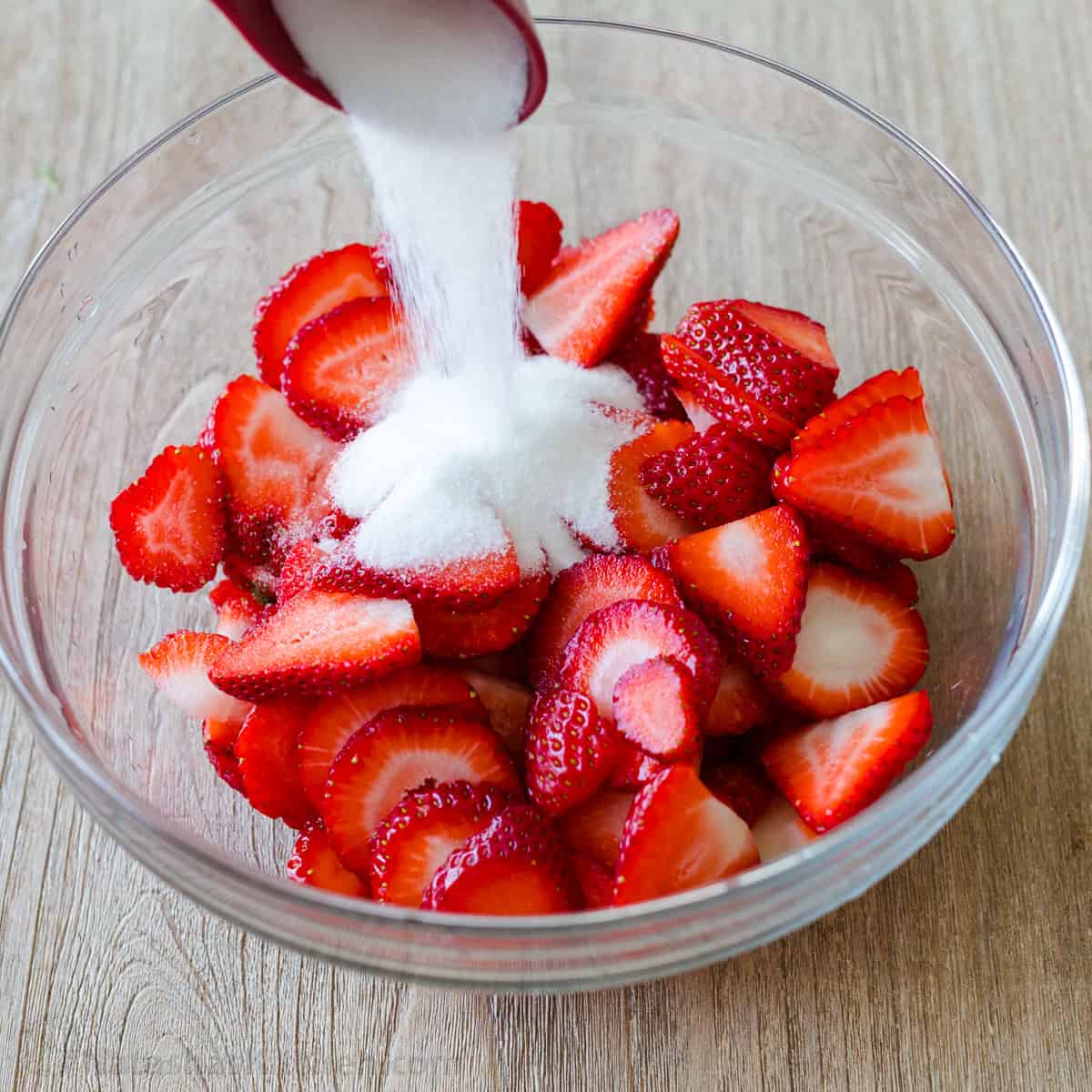 sugar poured into a bowl of strawberry slices for making macerated strawberries