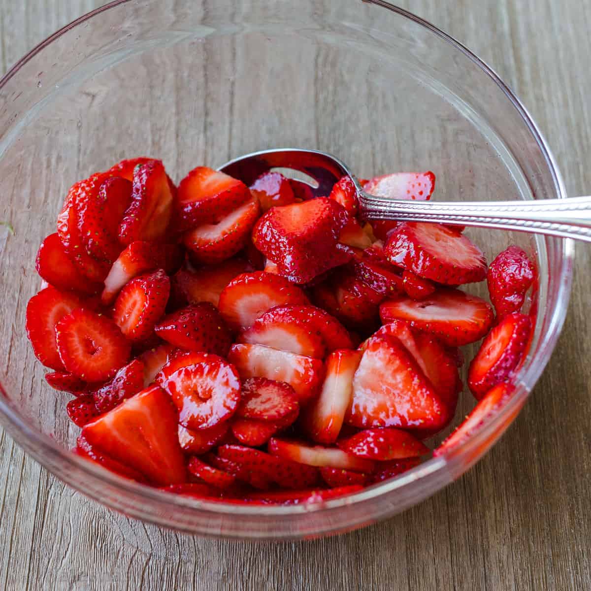 macerated strawberries in a clear bowl with spoon