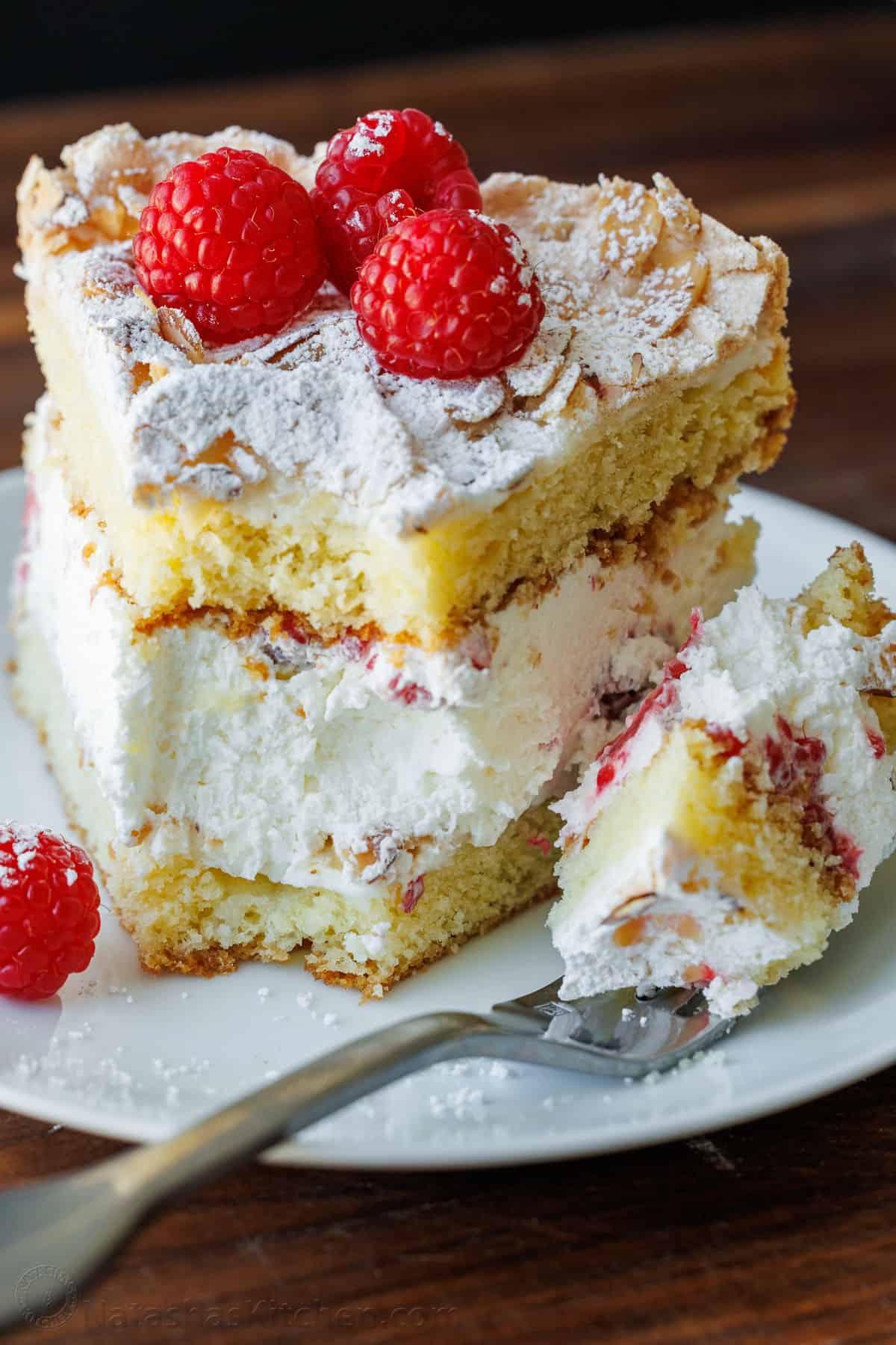 A slice of Himmelstorte on a plate with a bite loaded on a fork. Each slice shows the layered meringue, cake, and whipped cream