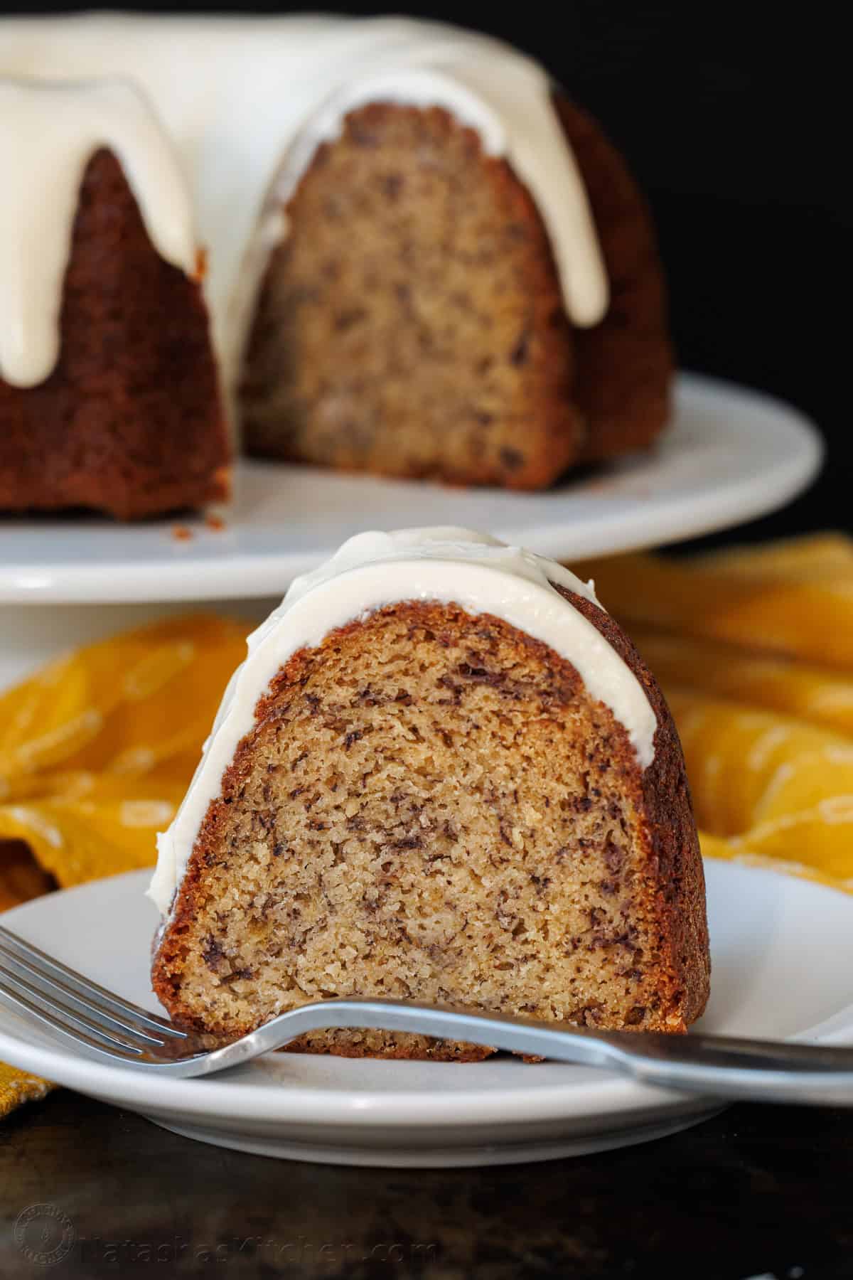 Slice of Banana Bundt Cake with cream cheese frosting on a plate with a fork